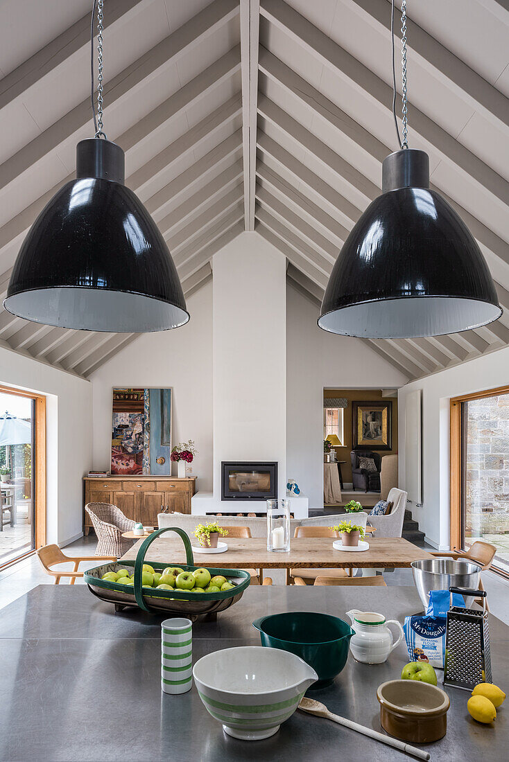 Utensils on kitchen island below pendant lights in open-plan interior with gable roof
