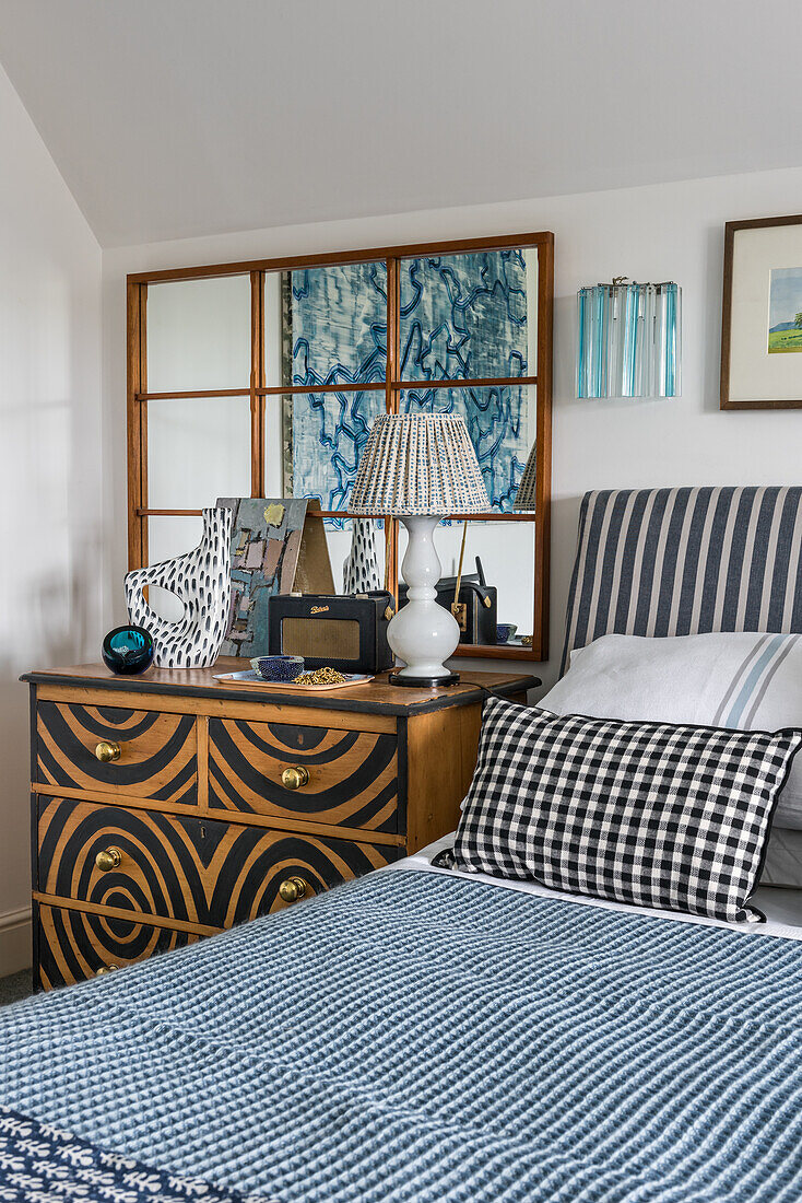 Bett mit blau-weißer Tagesdecke, daneben handbemalte Kommode und Wandspiegel