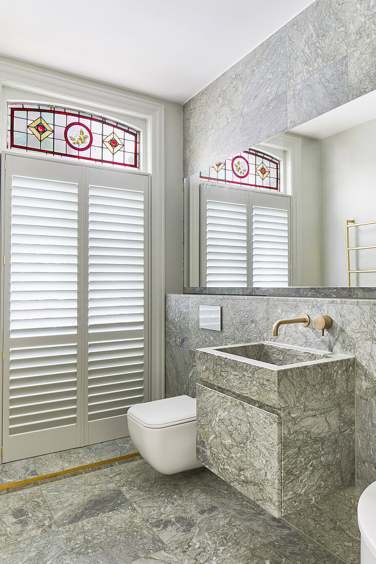 Sink next to toilet in bathroom with marble tiles, windows and stained glass elements