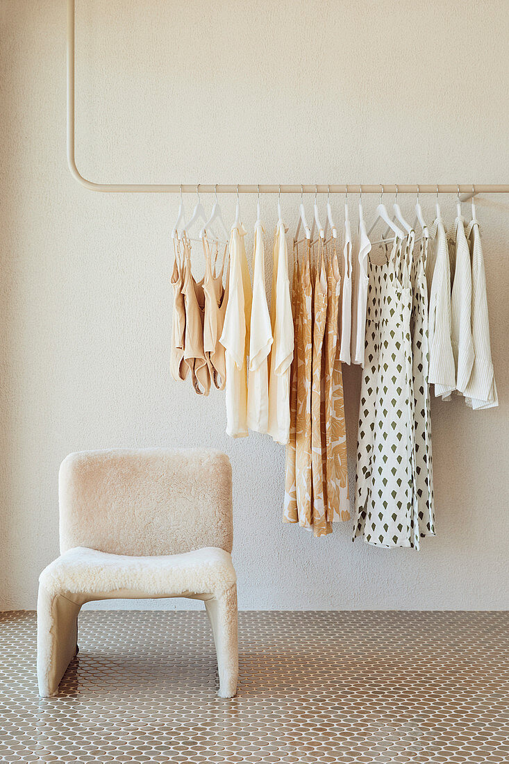 Women's clothes on rack with chair in front of it in bright interior