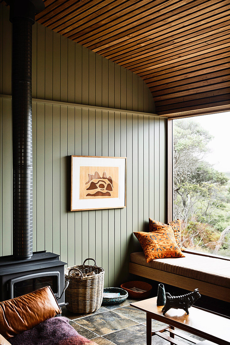 Seating area on window seat and wood-burning stove in room with green wood panelling
