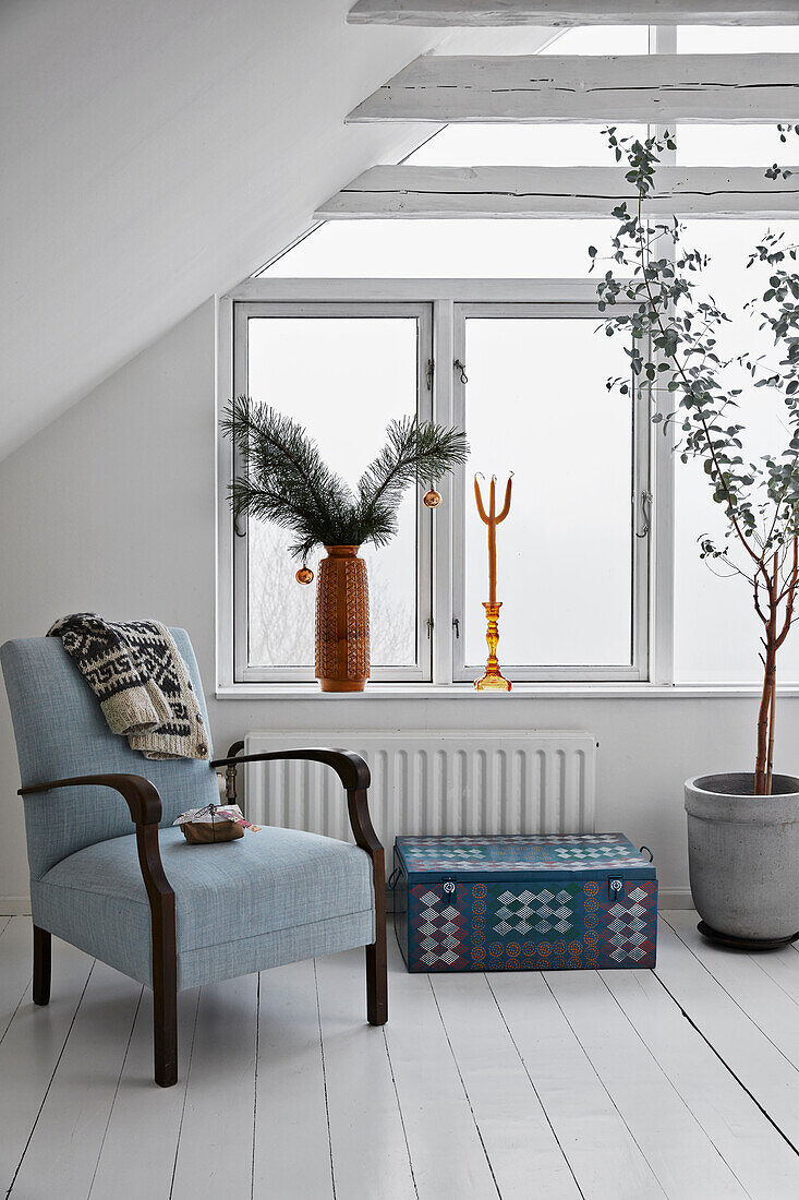 Old armchair, suitcase and tree house plant in the attic room with white floorboards, Christmas decorations on windowsill
