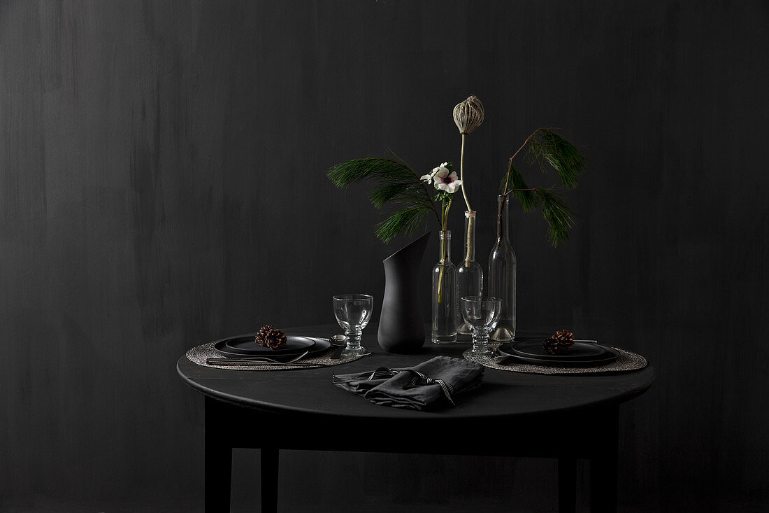 Schwarzer, gedeckter Tisch mit Lärchenzweig vor schwarzer Wand