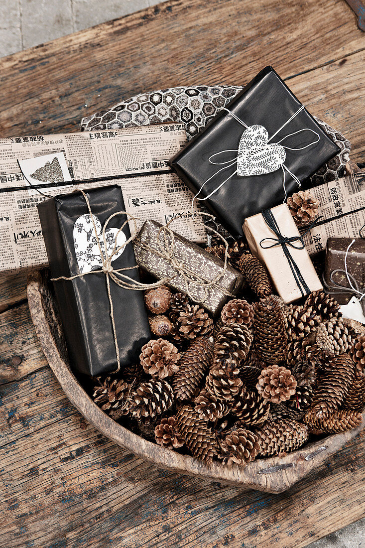 Verschiedene Zapfen und verpackte Geschenke in Holzschale auf rustikalem Holztisch