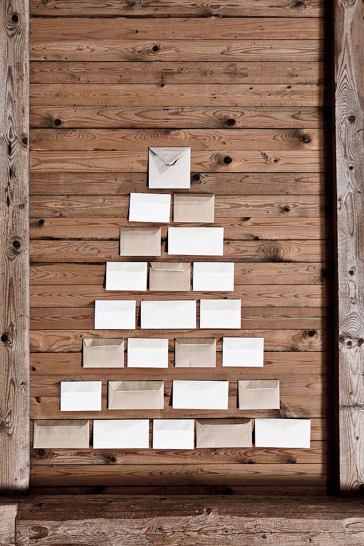 Envelopes arranged in shape of Christmas tree on rustic board wall