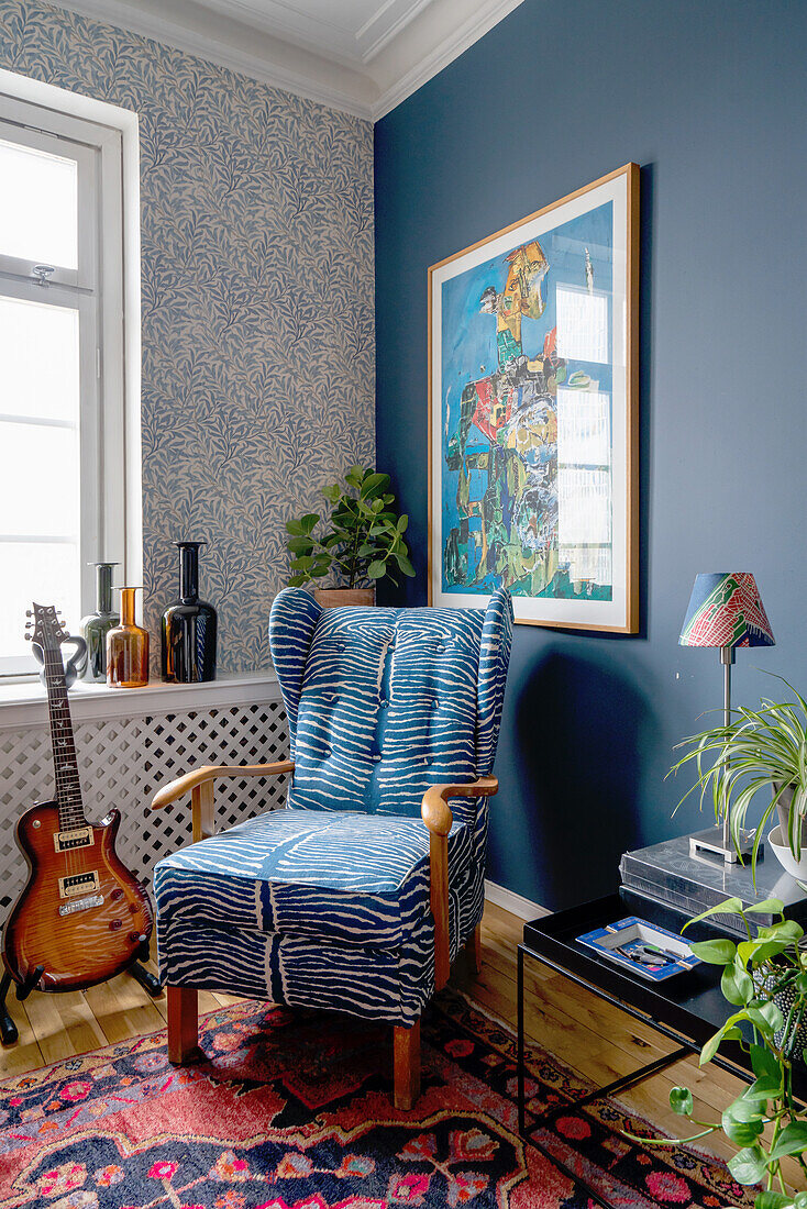 Wingback chair with animal print, guitar next to it in the room with walls in blue tones