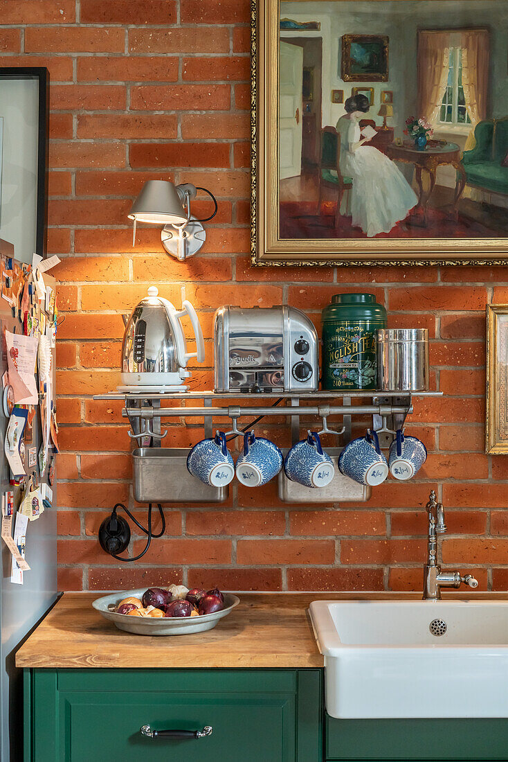 Shelf with cups and kitchen machines, above painting on an exposed brick wall