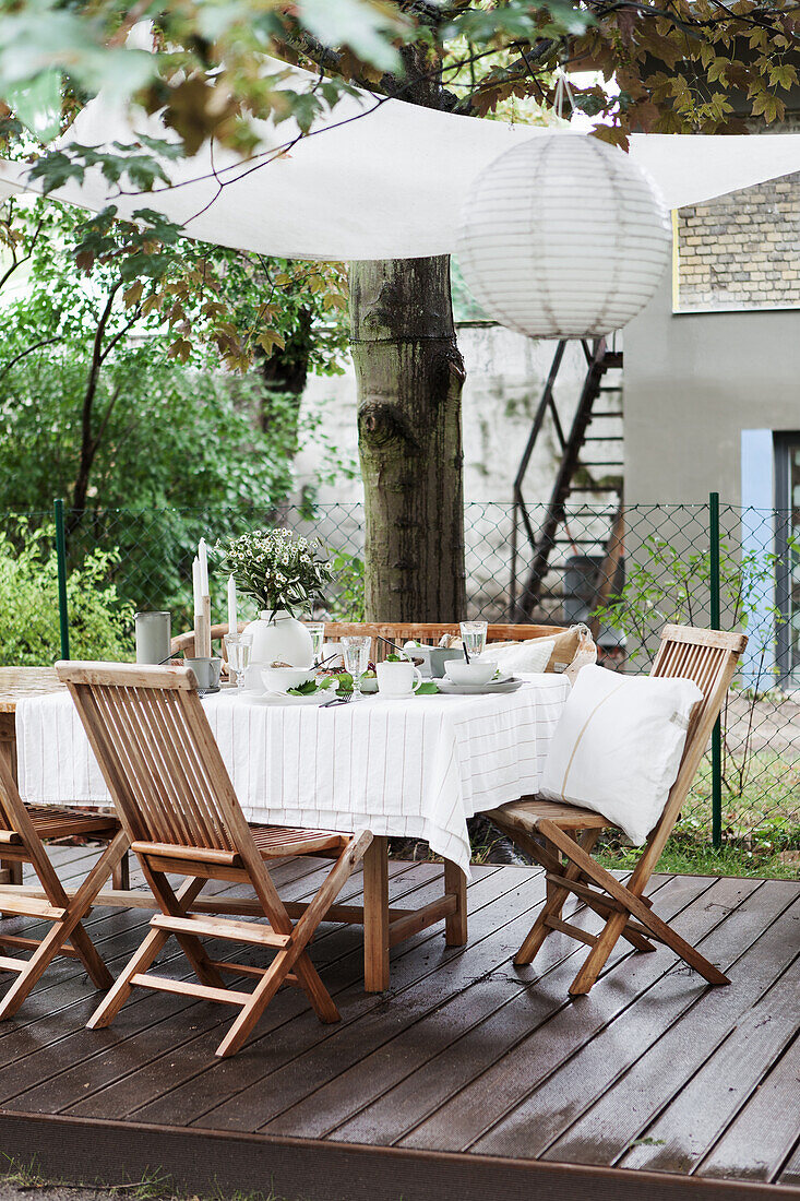 Gedeckter Tisch mit weißer Tischdecke und Stühle auf Holzterrasse