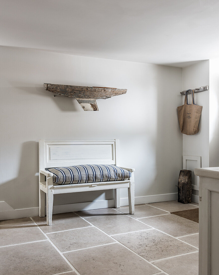 A driftwood boat on wall above antique bench with ticking stripe cushion, the floor tiles are limestone