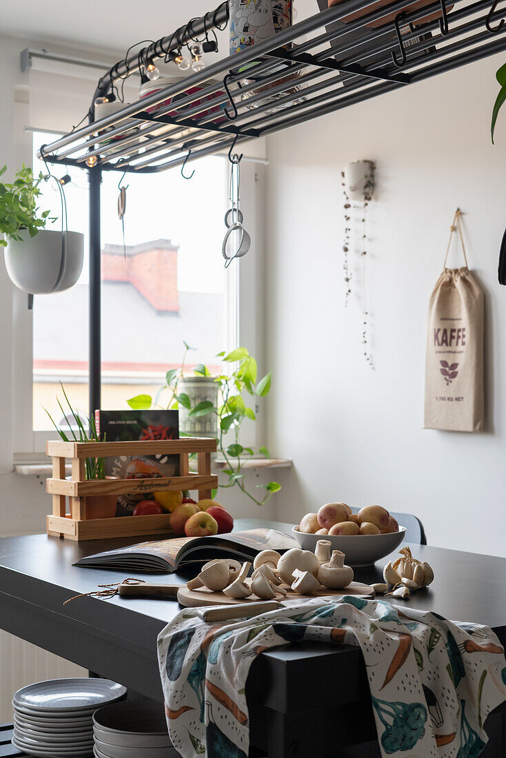 Mushrooms, potatoes, cookbook, and wooden crate on the kitchen island with a rack overhead