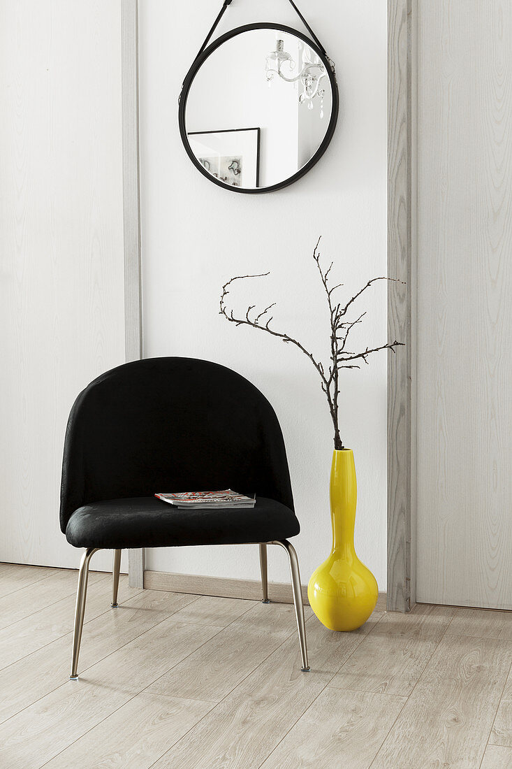 Zweig in gelber Vase neben schwarzem Stuhl, darüber Wandspiegel