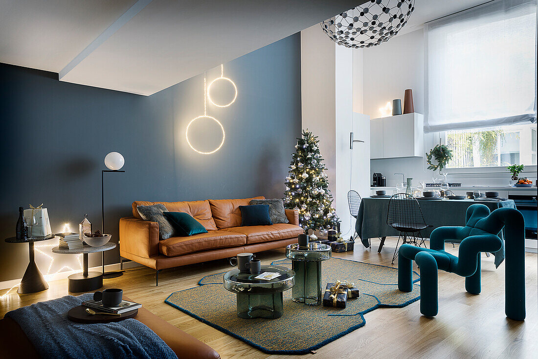 Ledersofa, Weihnachtsbaum und Designerstuhl im Wohnzimmer mit blauer Wand