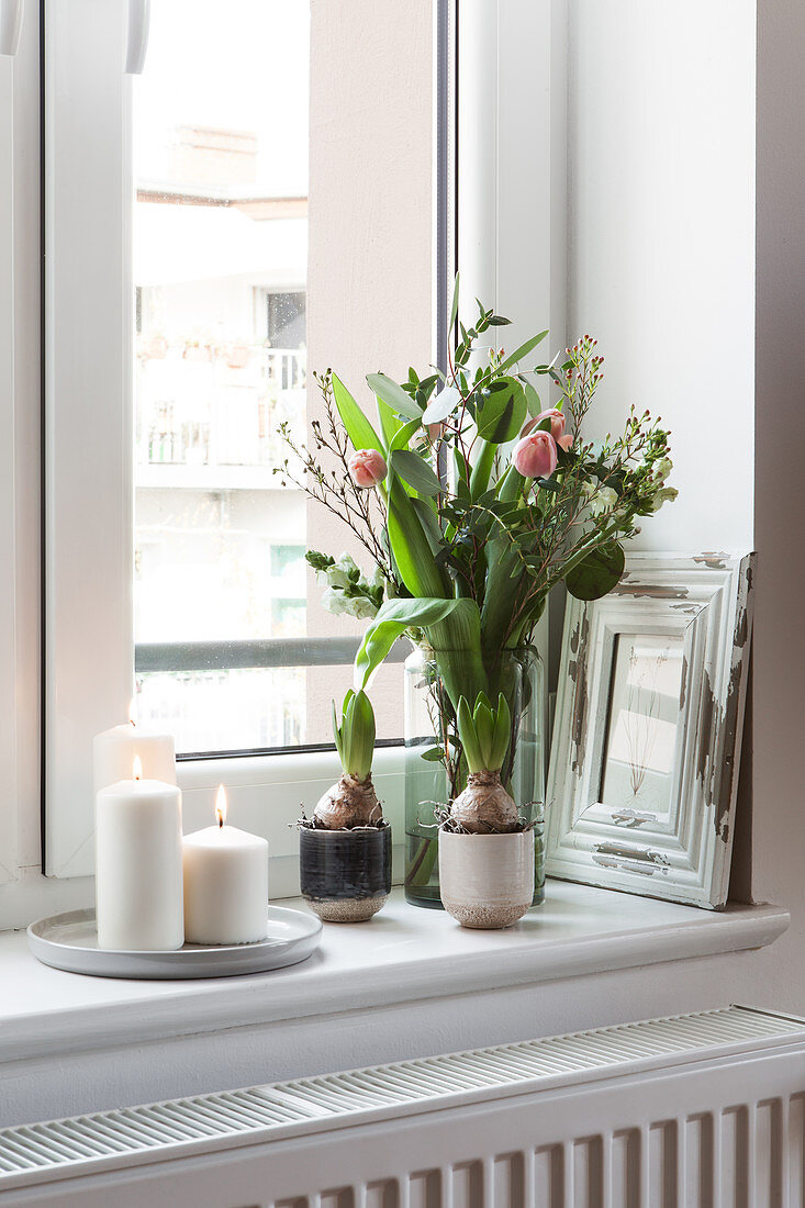 Frühlingsstrauß mit Tulpen und weiße Kerzen auf Fensterbank