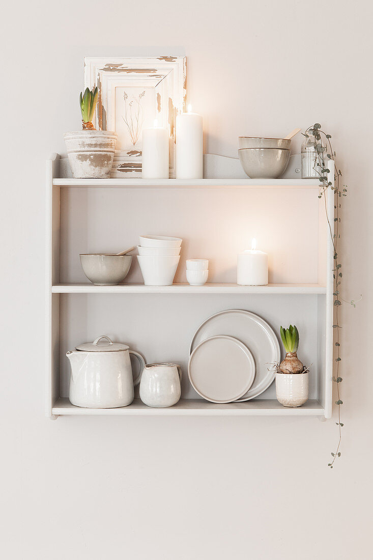 Crockery and white candles on wall-mounted shelves