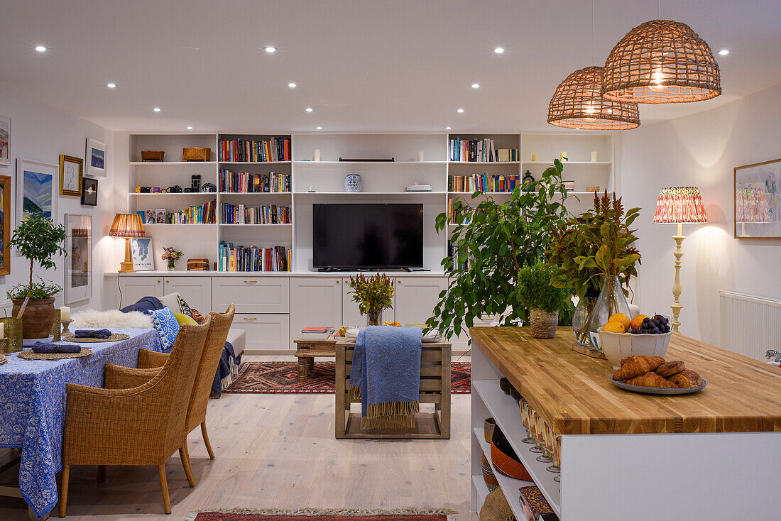Küchentheke mit Holzarbeitsplatte, Essbereich mit Rattanstühlen und Bücherwand mit TV in offenem Wohnraum