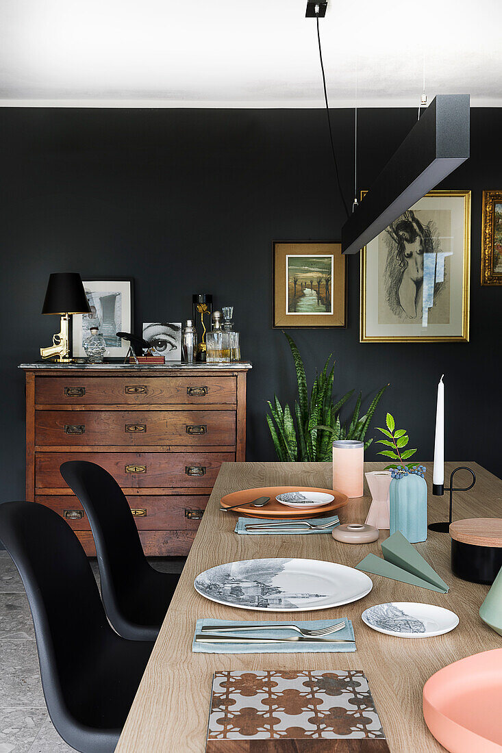Gedeckter Tisch mit schwarzen Stühlen, alte Holzkommode vor schwarzer Wand