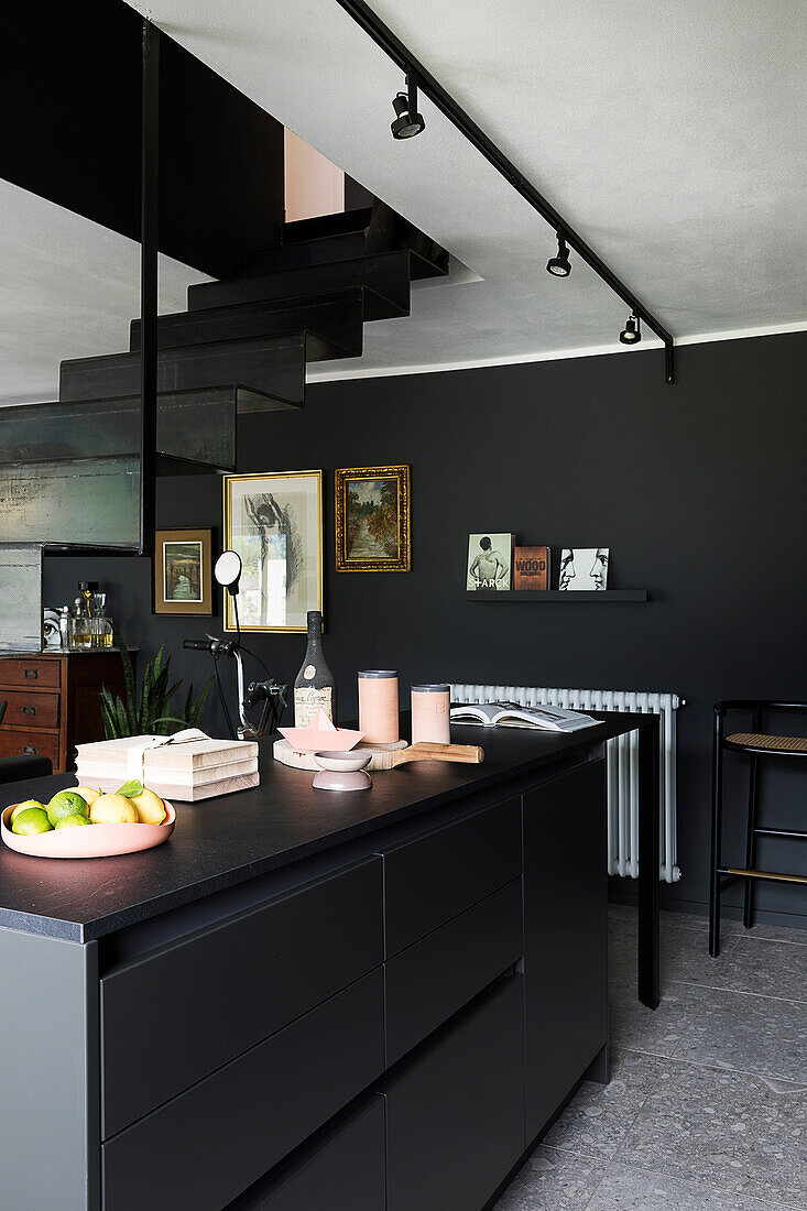 Black kitchen island in an open-plan living room with black walls and stairs to the gallery