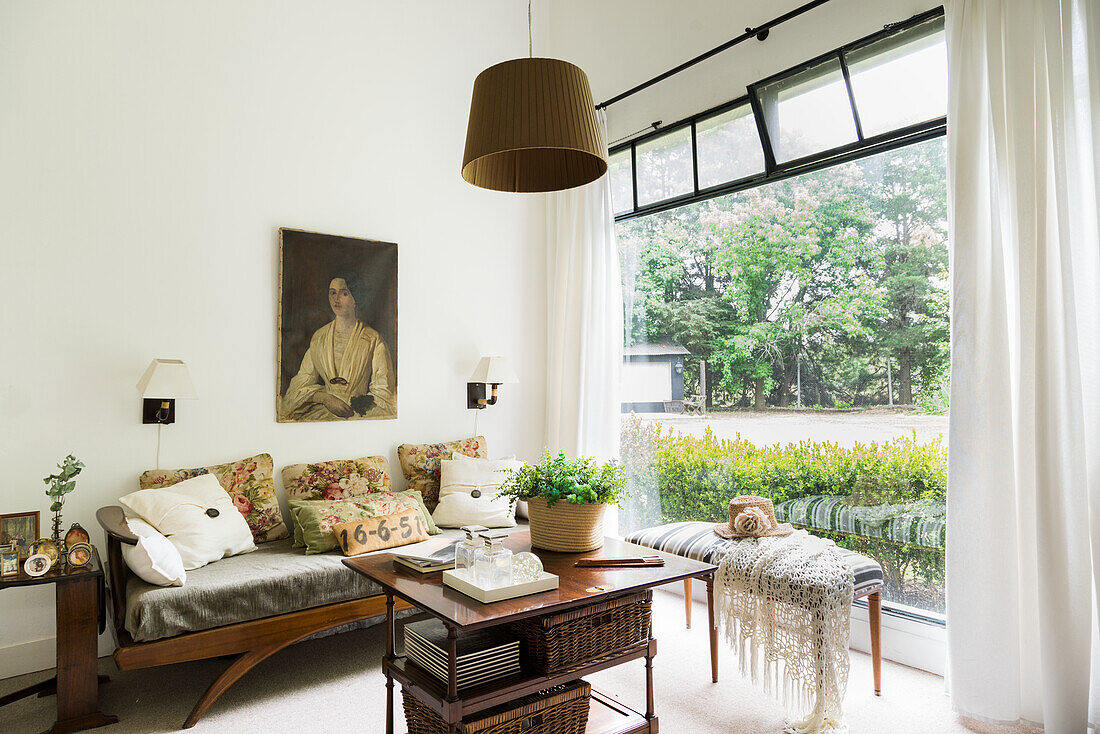 Sofa mit Kissen, darüber Frauenportrait, Tisch und Bank im Zimmer mit Gartenblick