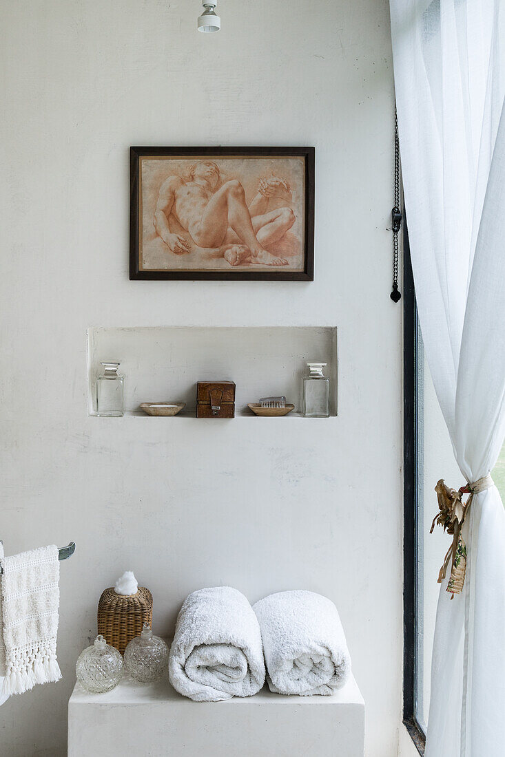 Handtuchrollen und Glasvasen auf Schränkchen, darüber Wandnische mit Dekoobjekten und Bild im Badezimmer