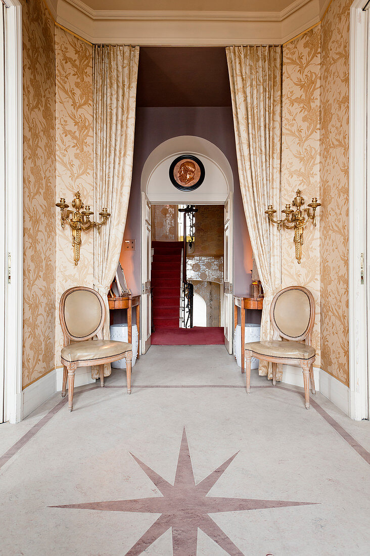 Pair of Louis-XVI-style dining chairs and gilt wall sconces in hallway with star inlaid in marble flooring