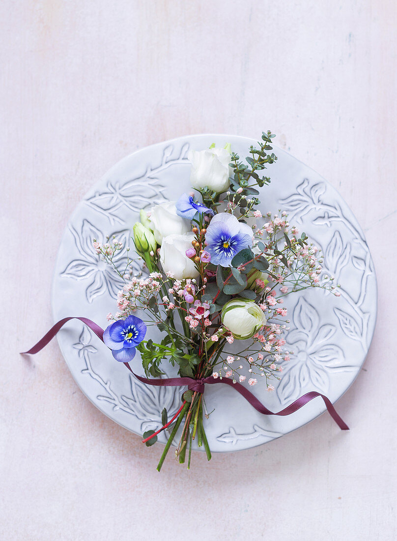 Spring posy of lisianthus, violas, waxflowers and eucalyptus decorating plate