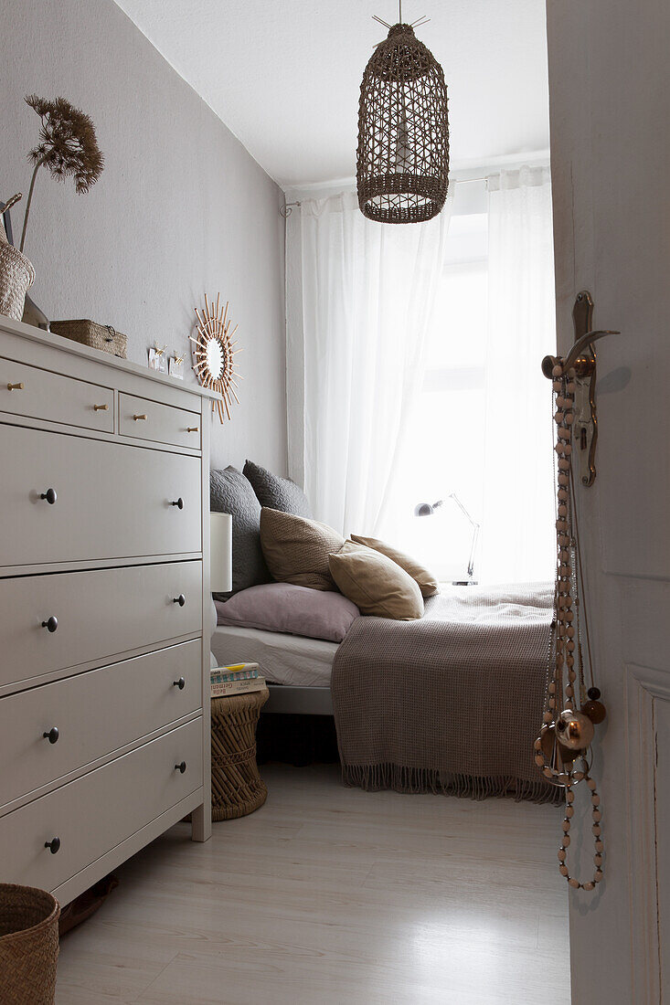 View through open door to white chest of drawers and bed in bedroom