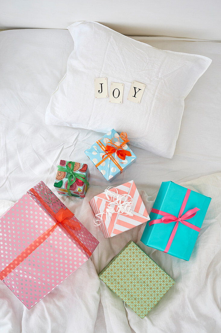 Multi-colored gift boxes on white bed and 'JOY' spelled with cards