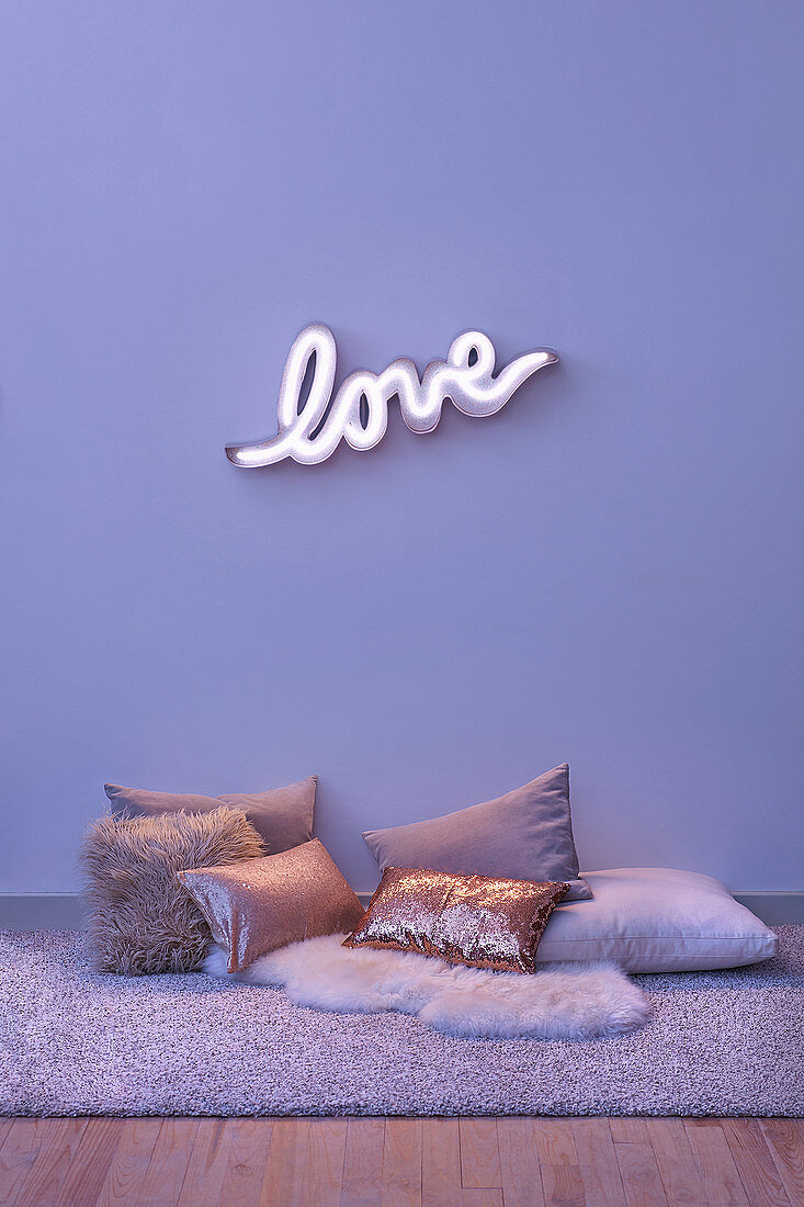 Neon wall light spelling 'LOVE' and various cushions on the floor