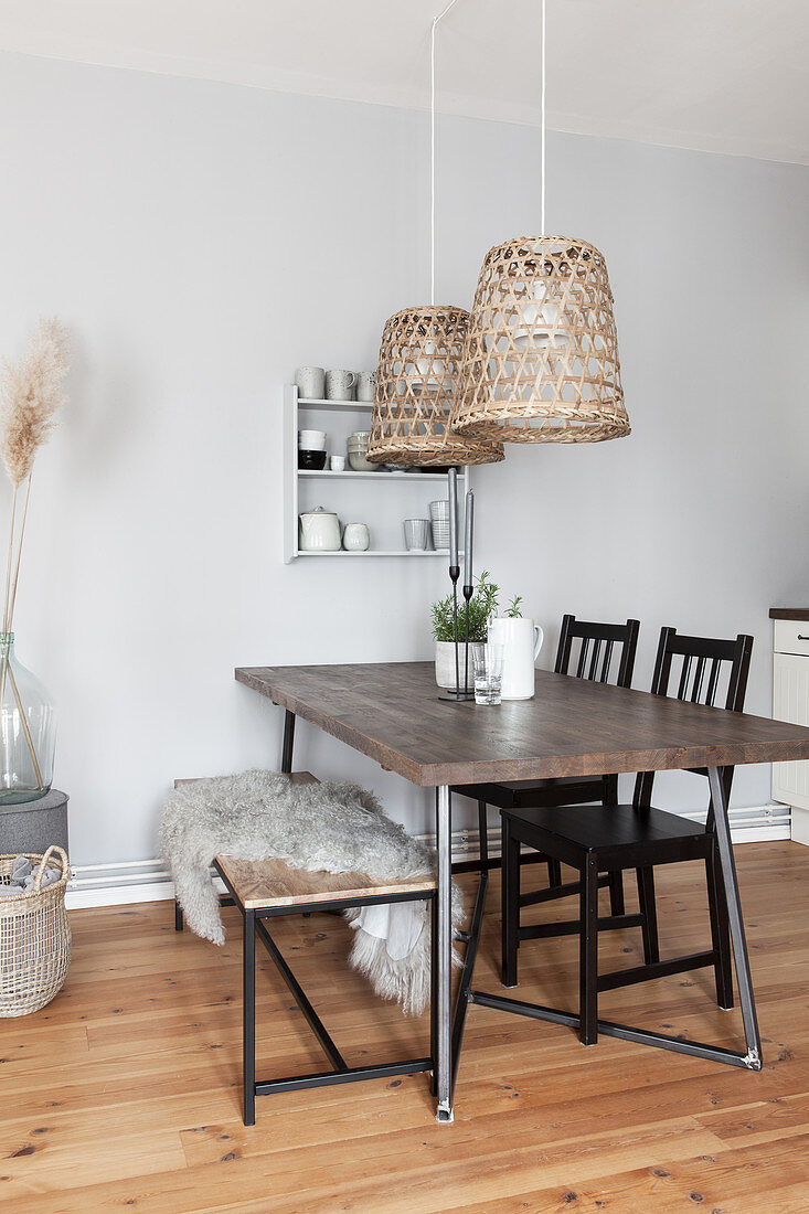 Dining table with dark wooden top, black chairs, fur blanket on bench and pendant lamps