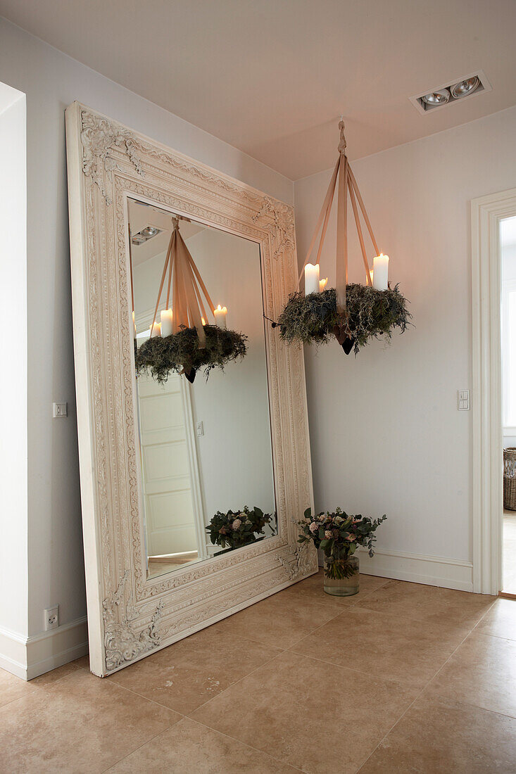 Hanging Christmas wreath with white candles and apricot-colored decorative ribbon in front of a large mirror