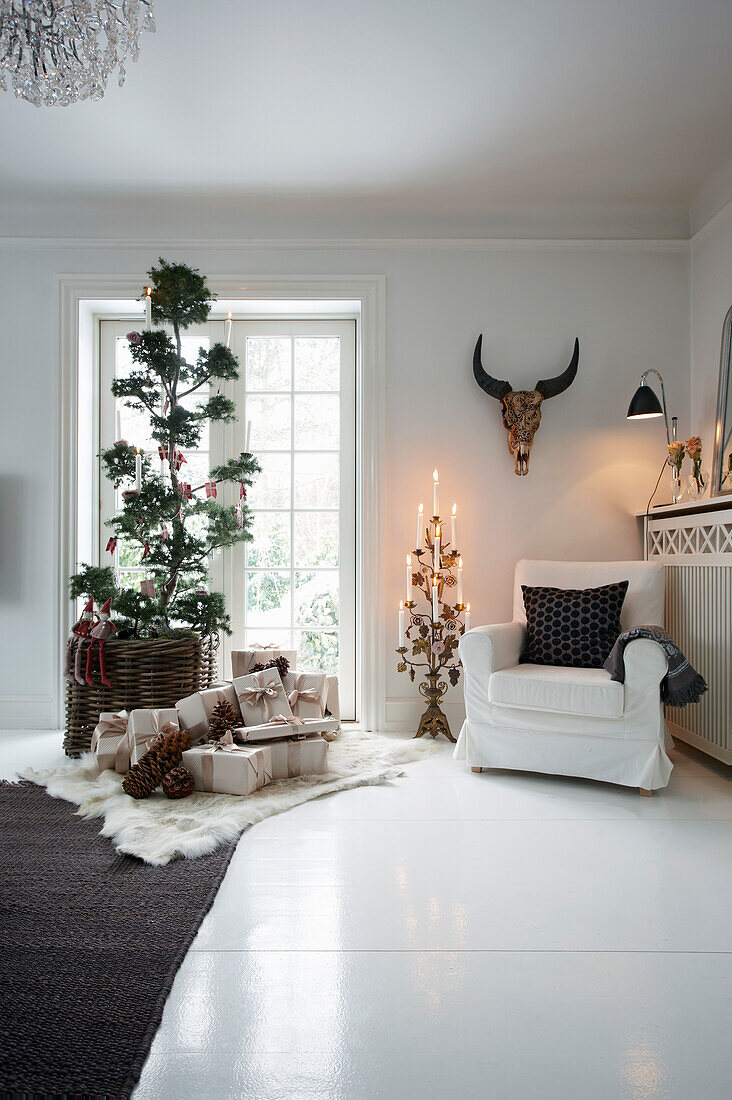 Geschmückter Baum, Weihnachtsgeschenke und Sessel im Wohnzimmer mit weißem Holzboden