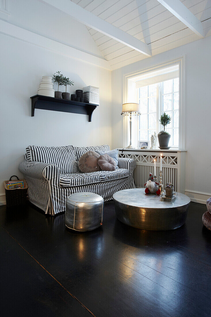 Sofa, coffee table and pouf seat in room with white walls and dark floorboards