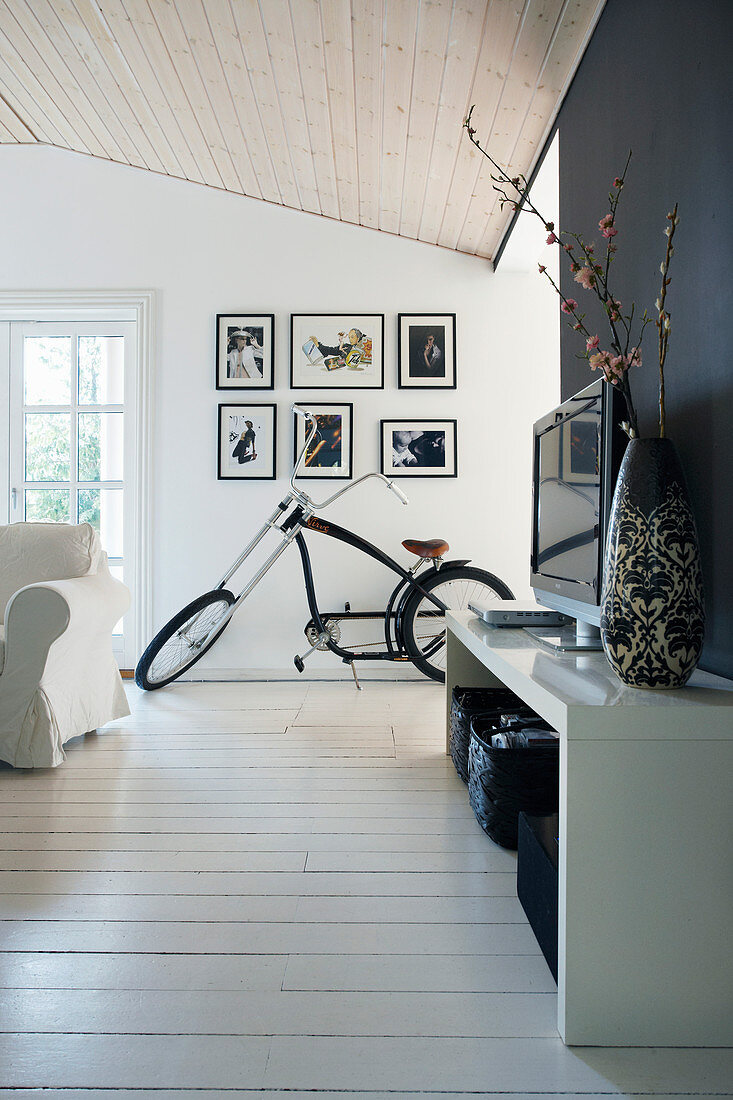 Fernsehregal und Fahrrad im Wohnzimmer mit weißem Dielenboden und teilweise schwarzer Wand