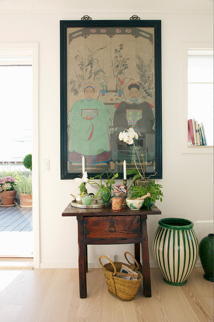 Plants on antique wooden table below Oriental artwork on wall