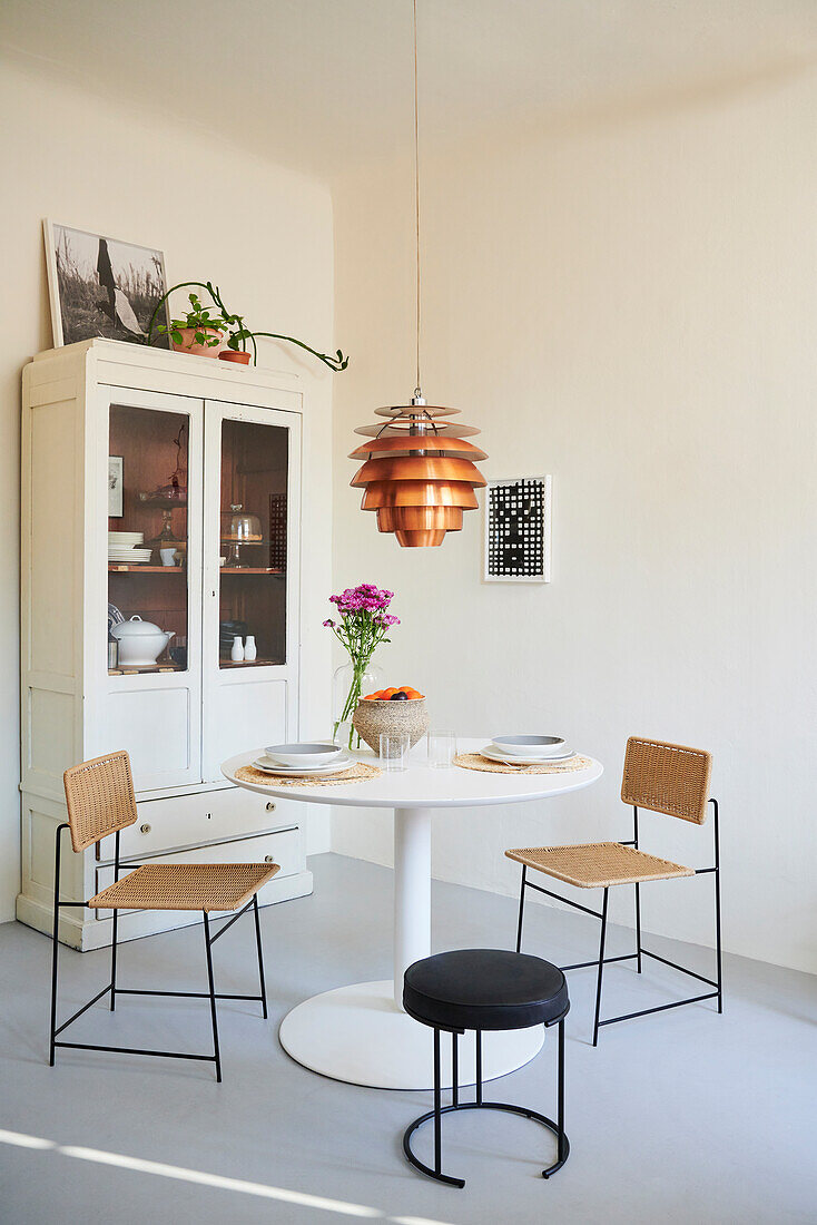 Round table with chairs, above it a copper lamp and cupboard in the corner of the room
