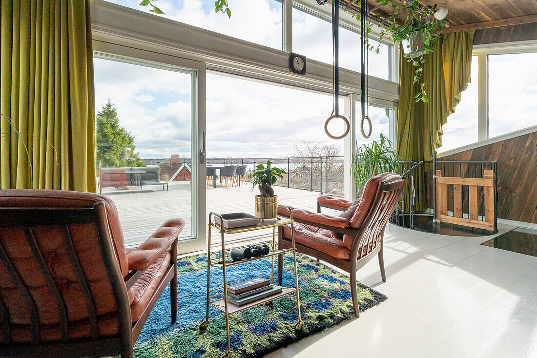 Armlehnstühle mit Lederauflage, darüber Turnringe im Wohnzimmer mit Glaswand und Terrassenblick