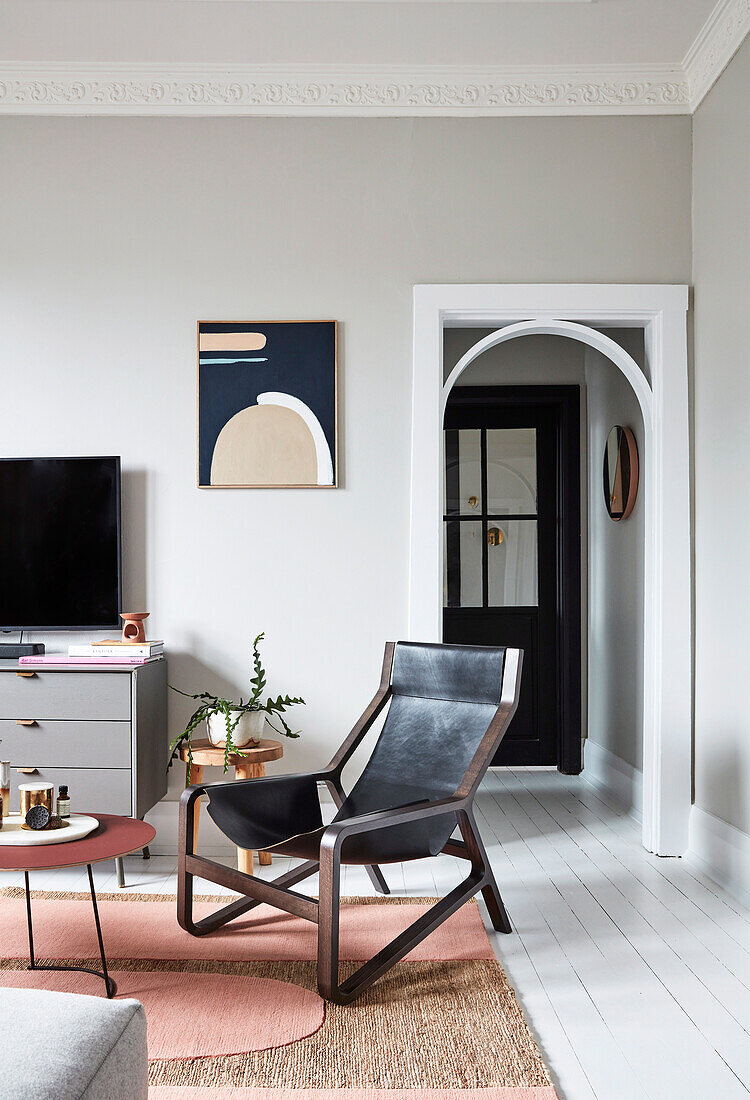 Schwarzer Lederstuhl im Wohnzimmer mit hellgrauen Wänden, Rundbogen-Durchgang zur Diele