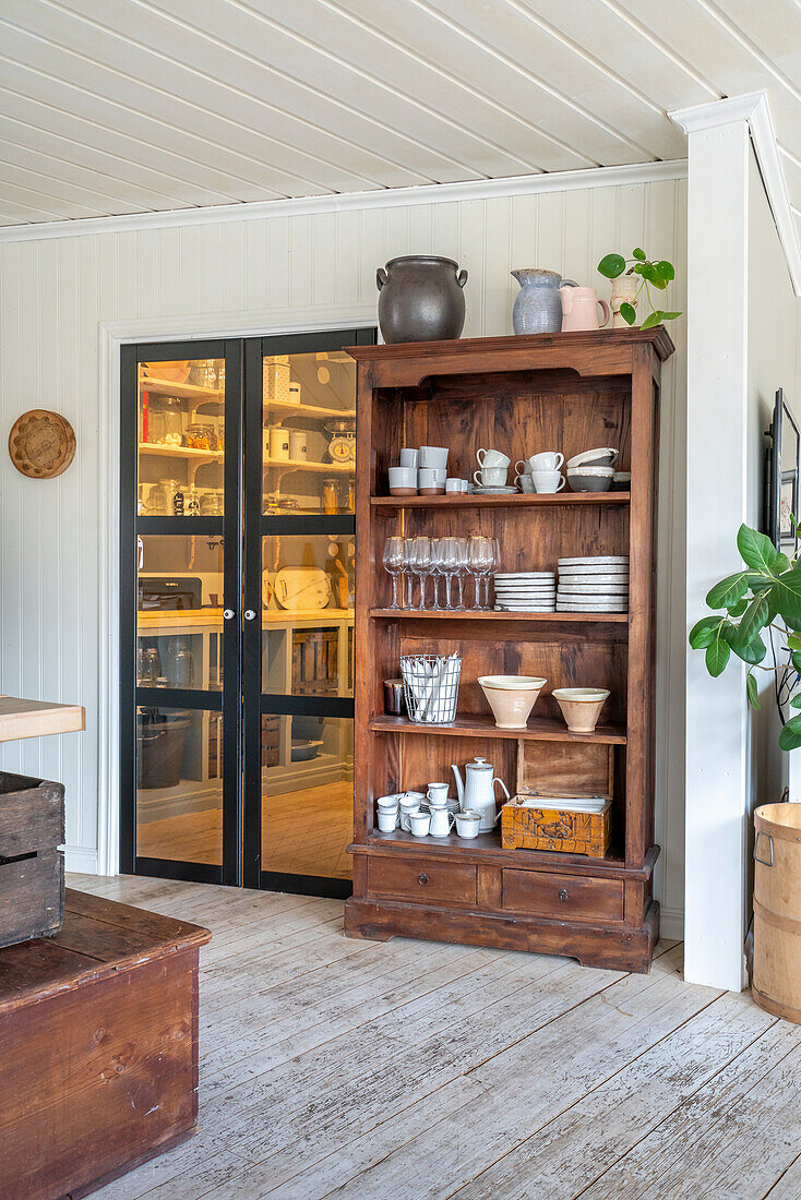 Open wooden crockery cupboard next to a glass door