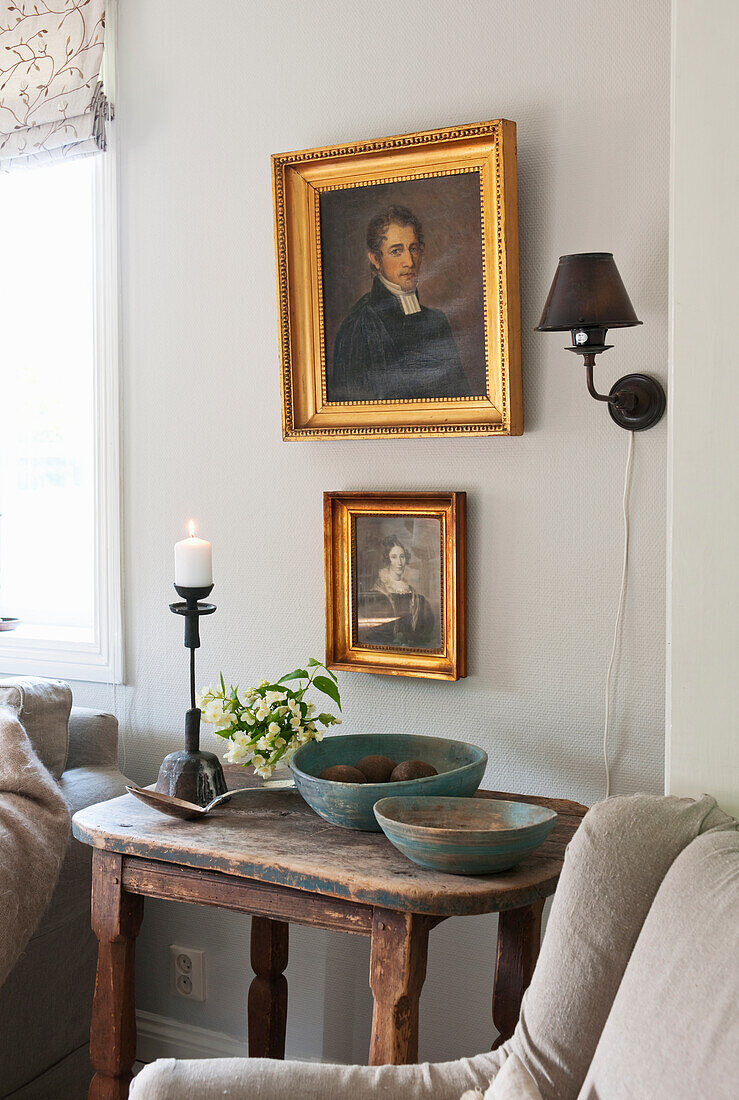Old wooden table, above it gold-framed portrait painting and wall lamp