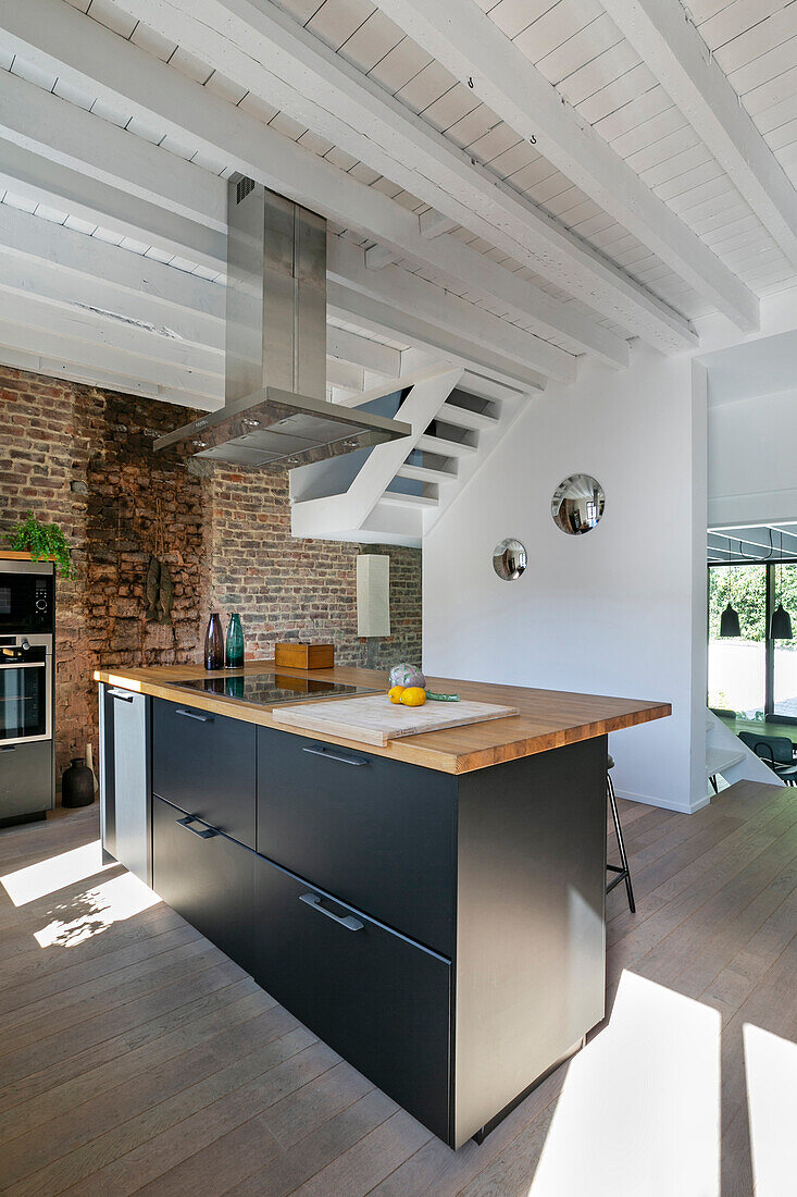 Modern kitchen island and extractor hood in loft apartment with brick wall