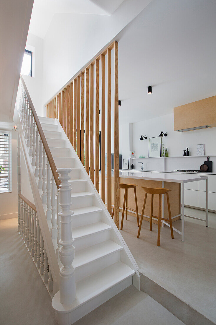 Treppenhaus mit weißen Treppen und offene Küche mit Kücheninsel, Holzsprossen als Raumteiler