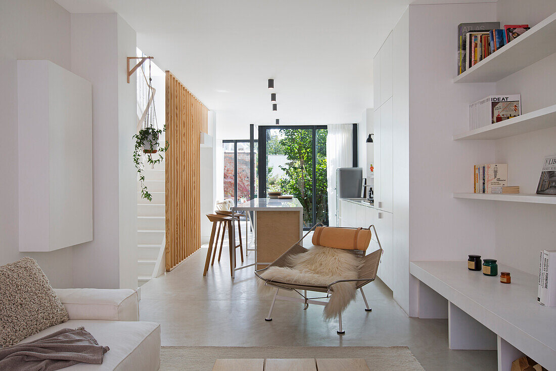 Weiße Regale und Klassiker-Liegestuhl in offenem Wohnraum, im Hintergrund Küche