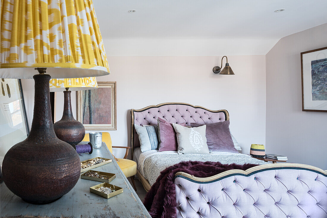Purple shearling throw on antique bed with buttoned headboard in guest room with pair of yellow ikat print lampshades
