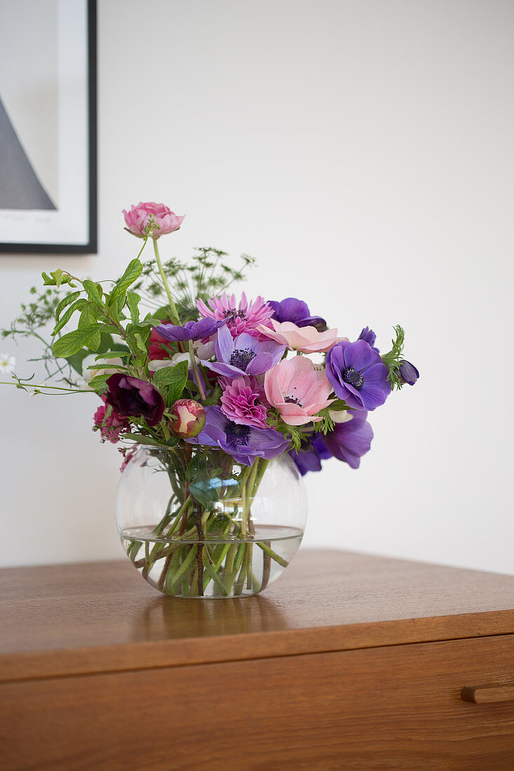 A bouquet of anemones in a glass vase on a chest of drawers