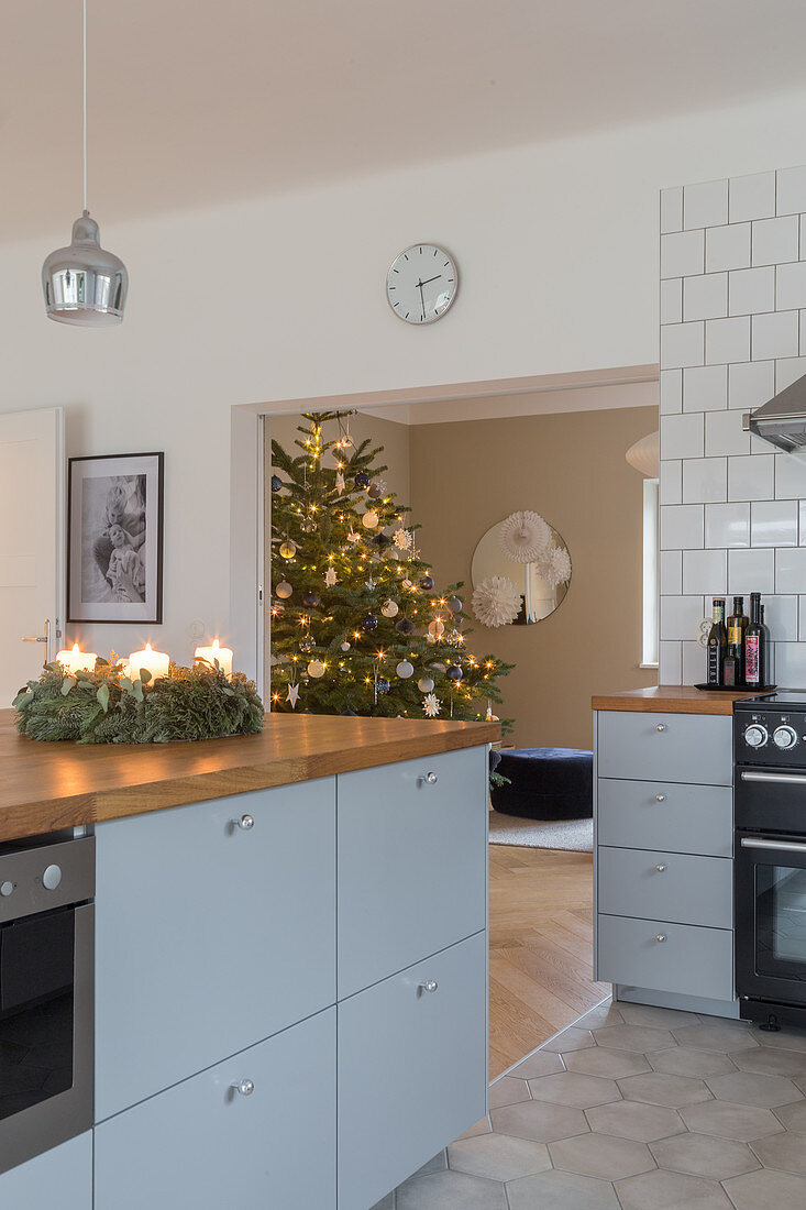 An Advent wreath on grey-blue kitchen island with a wooden worktop with a Christmas tree in the background