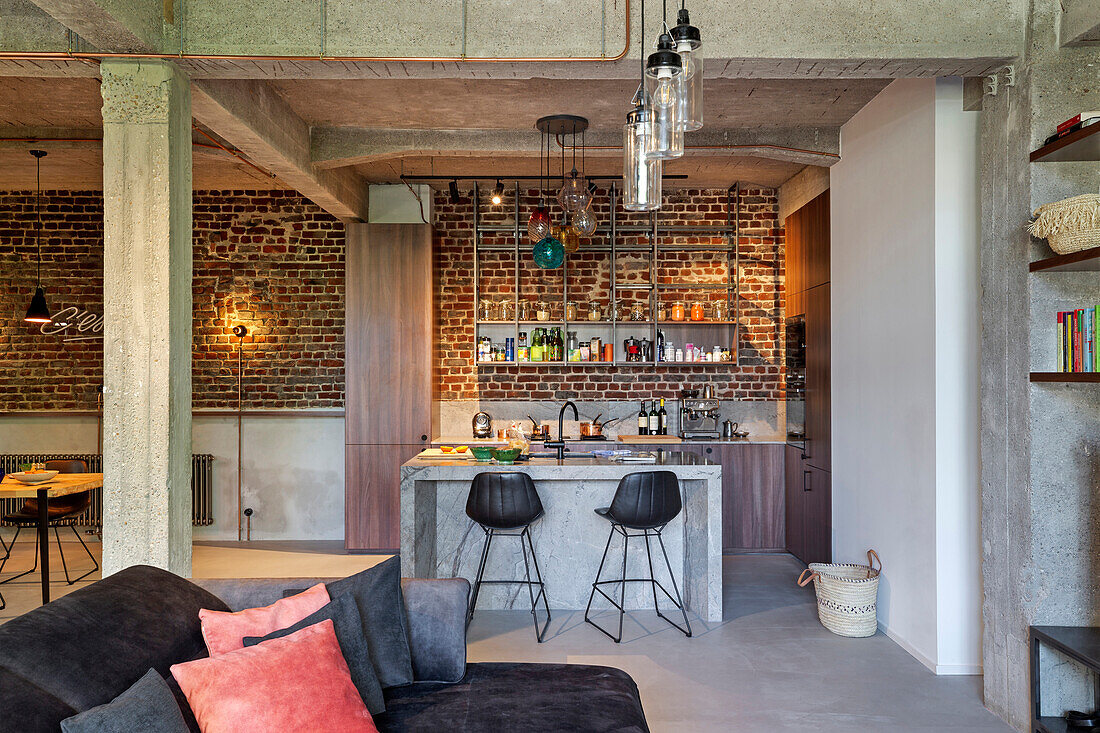 Open-plan interior of loft apartment with seating area in the foreground and kitchen with brick wall in the background