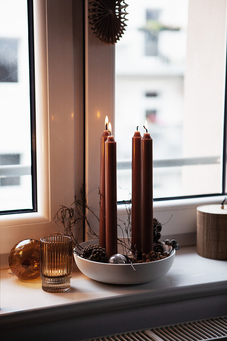 Bowl with cones and candles on windowsill