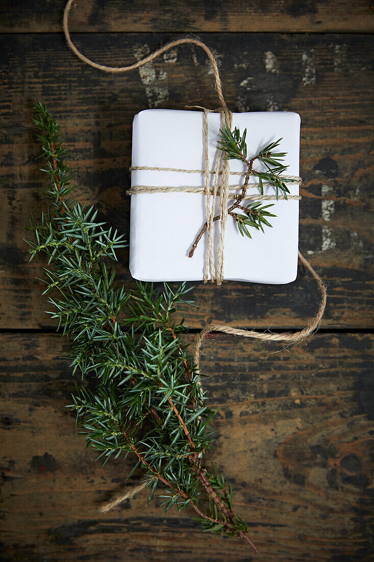 Weiß verpacktes Geschenk als Adventskalender mit Wacholderwzeigen dekoriert