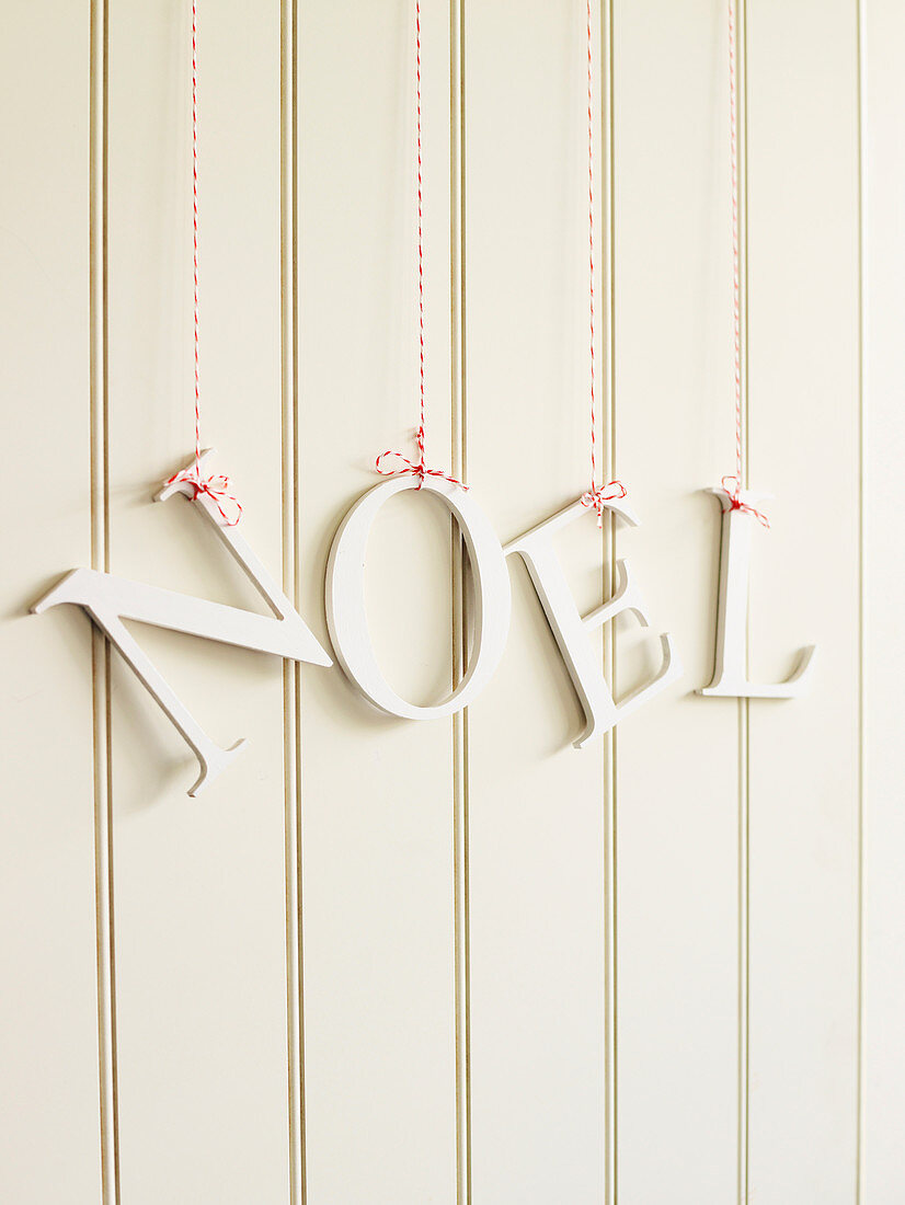 Decorative letters reading 'NOEL' hung from red and white strings on white wooden wall