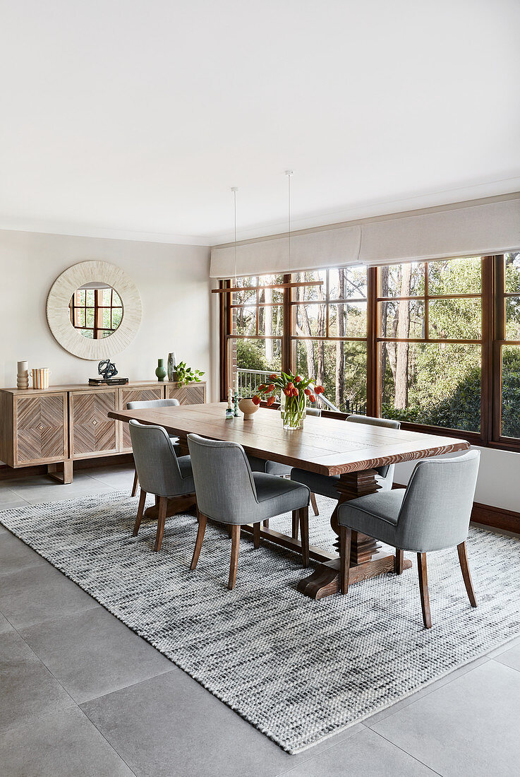 Esstisch aus Holz mit grauen, gepolsterten Stühlen vor Fenster